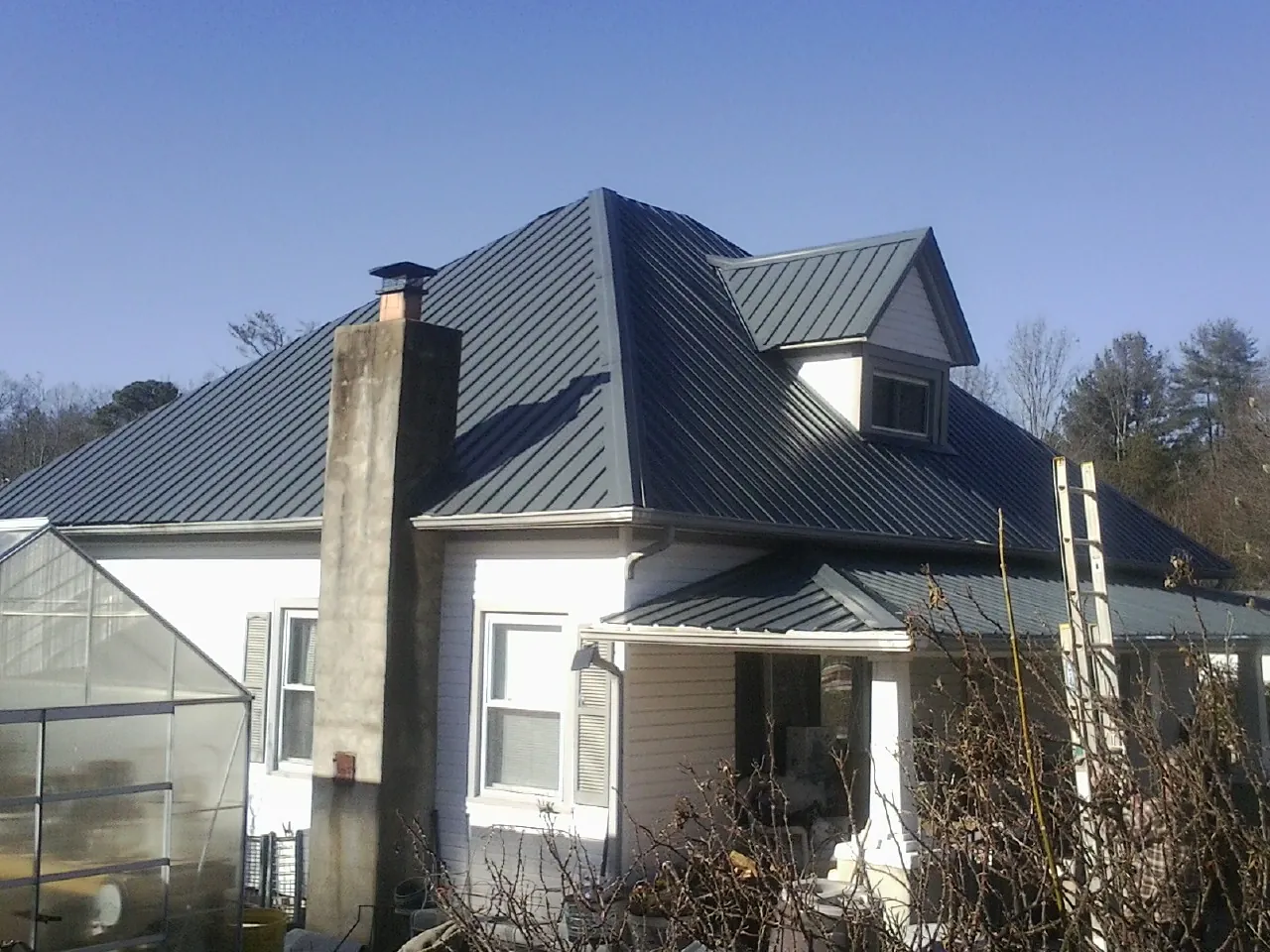 Dark blue standing seam metal roof on a white farmhouse with dormer — Slate & Tile Roof Repair by Roofing Brothers in Inman