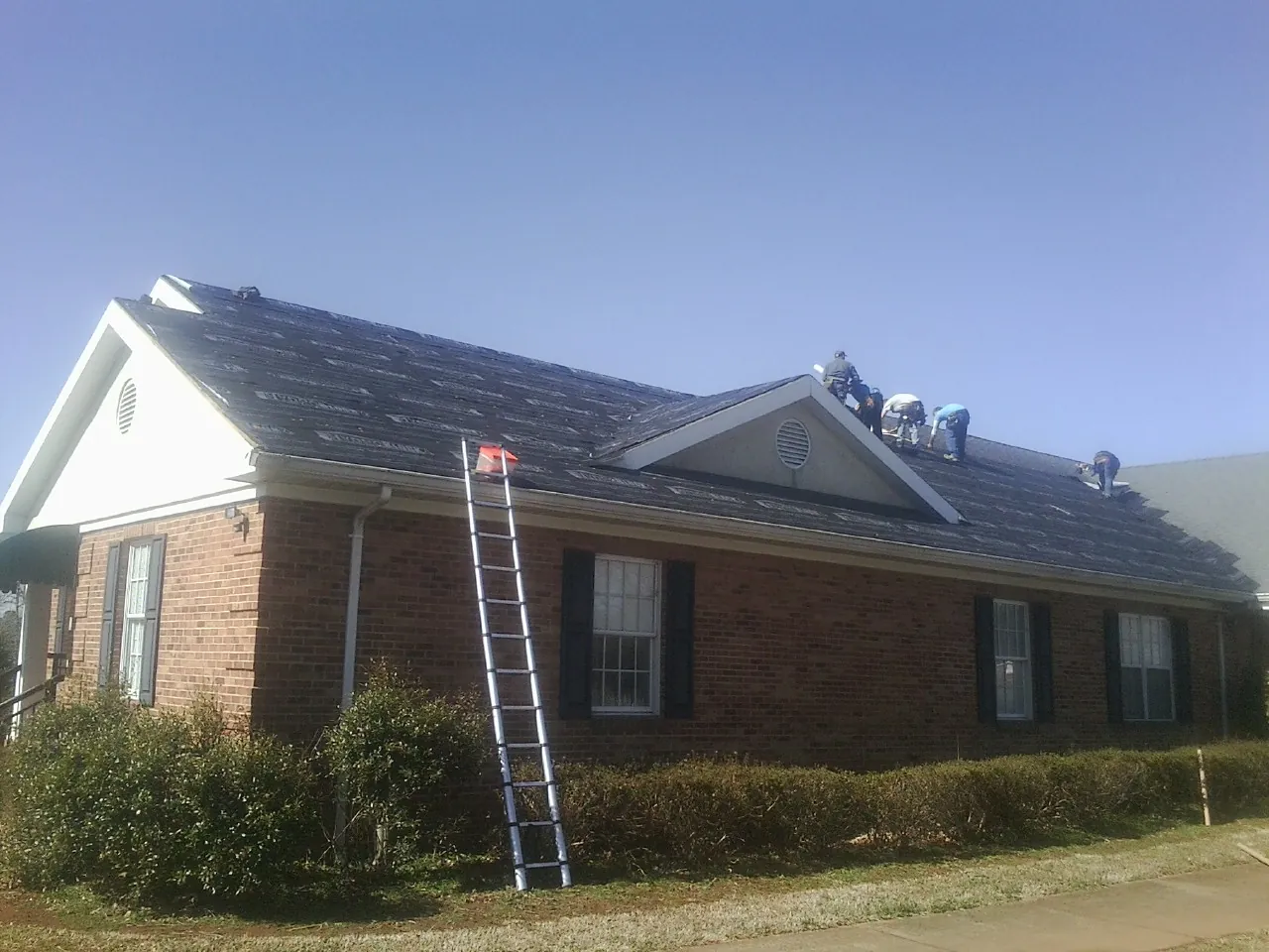 Crew tearing shingles off a brick ranch roof with a ladder set — Emergency Roof Repair work by our crew in Inman