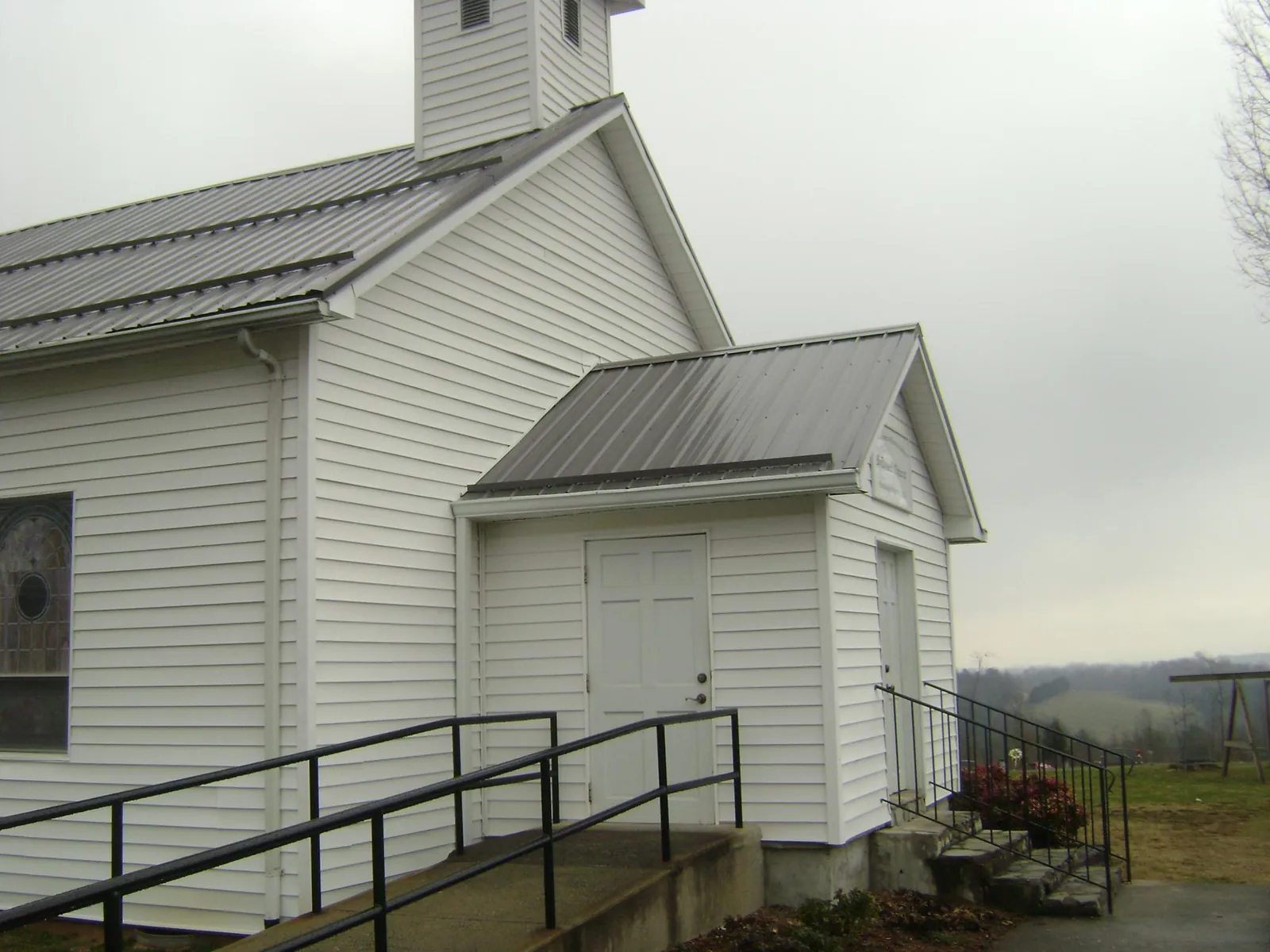 Gray metal roof on a white clapboard church with a steeple in Inman