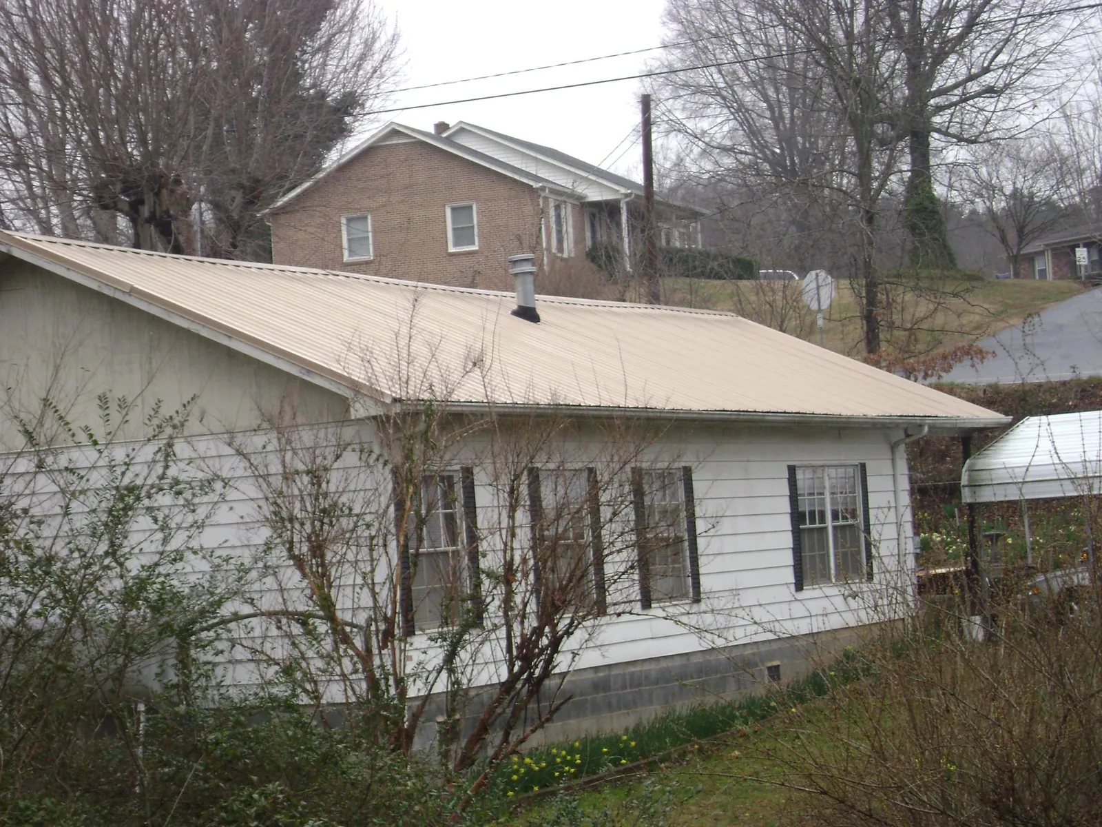 Tan metal roof on a white sided house set into a hillside — Commercial Roofing by Roofing Brothers in Inman